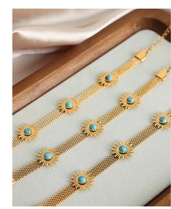 Detail of 18k gold mesh bracelets featuring turquoise sunflower charms on silk background