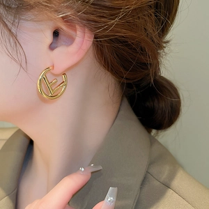Close-up of golden metal letter E earrings worn by a model for a chic commute style