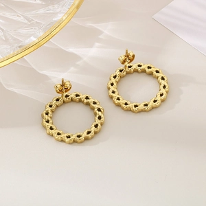 Close-up of golden geometric twisted oval earrings with intricate chain texture on white fabric