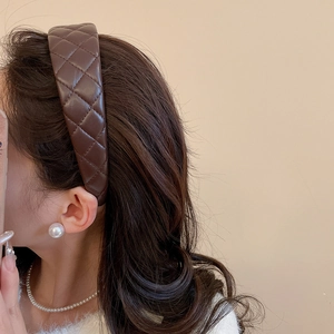 Detail view of a dark brown quilted faux leather headband worn on a model's head