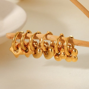 Detailed close-up of gold stainless steel heart and flower pendant earrings on a wood stand