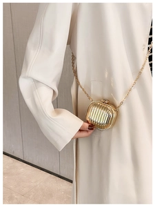 Detail of mini gold metallic crossbody bag with pleated texture on white coat