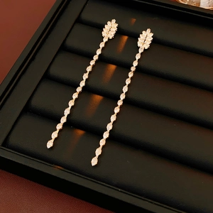Detailed view of golden leaf tassel earrings with white zircons in a black jewelry box