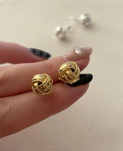 Primer plano de pequeños pendientes de nudo trenzado dorado con textura vintage