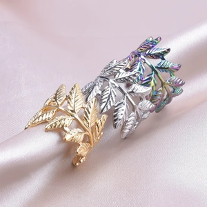 Macro shot of three leaf-shaped rings in gold, silver, and rainbow on pink satin fabric