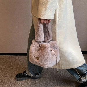Niche purple plush bucket bag with gold chain strap shown worn with a beige coat