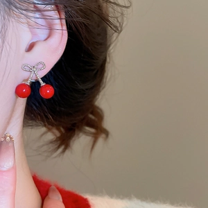 Close-up of model wearing silver bow cherry earrings with red beads and woven texture