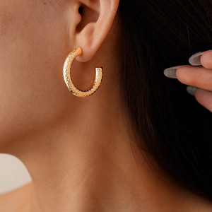 Macro detail of golden C-shaped hoop earring with unique hammered spotted texture on model