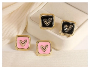 Dettaglio di orecchini a lobo quadrati placcati oro con cuori in smalto nero e rosa