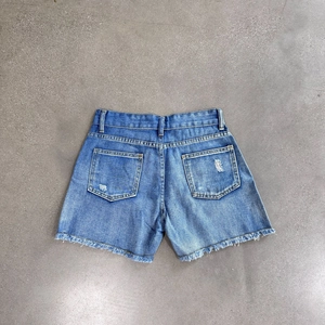 Detail of distressed back pockets and raw fringe hem on blue denim shorts