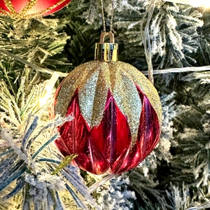 Close-up of red and gold Christmas ball with glitter and wave texture on a snowy tree