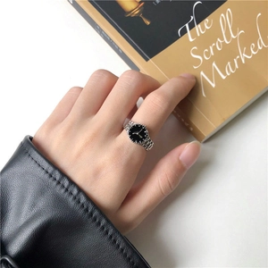 Detail of creative silver watch-shaped ring with black dial worn on finger by a book