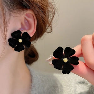 Macro detail of black flocked floral earrings with gold center accents and velvet texture