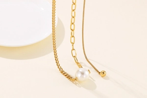 Macro detail of gold-plated necklace featuring a white pearl pendant and mixed chain link