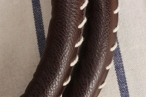 Detailed close-up of dark brown lychee leather handbag handle with hand whipstitch