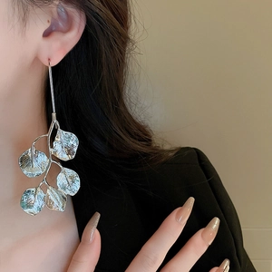 Detailed view of silver leaf branch earring worn by a model in warm soft lighting