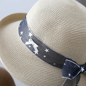 Detail of woven straw hat featuring star-patterned navy ribbon and white bow accent