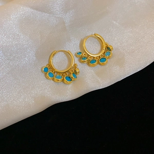 Close-up of golden hoop earrings with turquoise stones on white silk fabric background