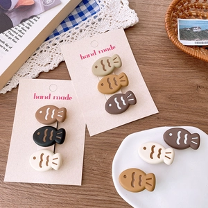 Set of 9 cute cartoon fish hair clips in matte earth tones on a vintage desk