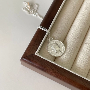 Silver vintage 1969 coin pendant necklace displayed on a wooden jewelry display box
