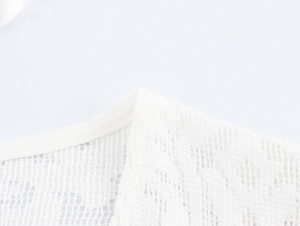 Nahaufnahme der weiß halbtransparenten Strickwaren-Textur und der Netz-Saumkante am Kleid
