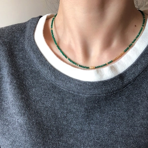 Detail of green beaded necklace with gold metal accents worn by model in close-up shot