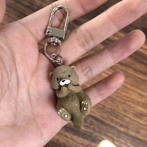 Close-up of a cute brown resin otter keychain charm being held over a wooden background