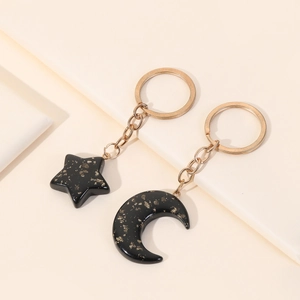 Detail of star and moon acrylic couple keychain with golden glitter on warm background