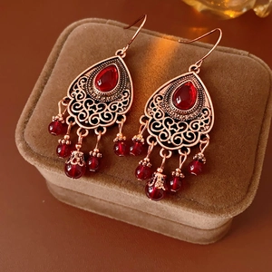 Dettaglio macro di orecchini boho in bronzo con gemme rosse e trama in filigrana