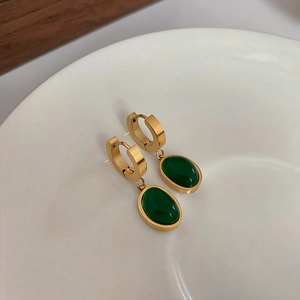 Macro shot of minimalist gold hoop earrings featuring polished green oval gemstone drops