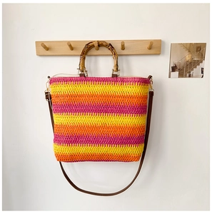 Detail of colorful woven straw bag with bamboo handles and striped sunset pattern