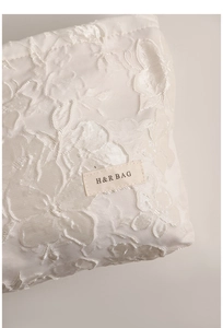 Macro detail of white floral embossed jacquard fabric with elegant H&R BAG cloth label