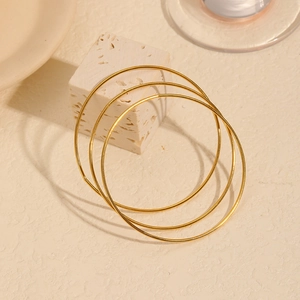 Drei minimalistische 18k vergoldete Edelstahl Armreifen auf Steinhintergrund