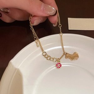 Detail of gold chain bracelet featuring horse charm and red cross coin on white ceramic