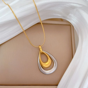 Macro shot of double-layer gold and silver teardrop pendant on a gold snake chain