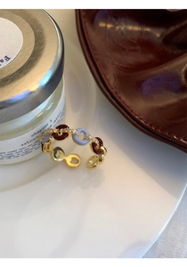 Detail of gold zircon ring with red and purple enamel links on a minimalist white tray
