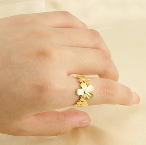 Detalle de un anillo de flor en oro de 18k sobre tela de seda beige en la mano de un modelo