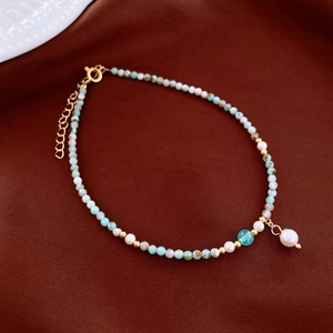Detail of Amazonite beaded anklet with white pearl and gold clasp on brown fabric