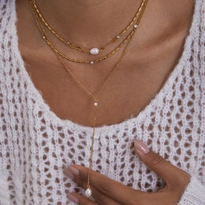 Detail of layered gold titanium steel necklace with cross, pearls and Y-shaped chain on model