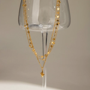 Detailansicht der mehrlagigen Goldhalskette mit Sternanhänger an einem Glas drapiert