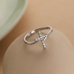 Silver-plated zircon cross open ring displayed on a smooth beige stone surface