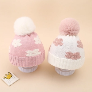 Close-up of winter baby knit hats featuring floral jacquard patterns and large faux fur pom-poms