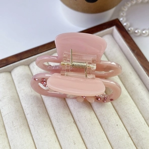 Close-up of a pink acetate hair claw clip with rhinestones and flower detail in a jewelry box
