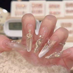 Luxurious almond nails with gold snake, butterfly charms and pearls in glossy nude finish