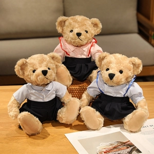 Three plush teddy bears in preppy outfits including pink and blue shirts on a wooden table