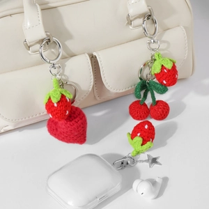 Handmade crochet strawberry and cherry keychains hanging on a beige bag and earbud case
