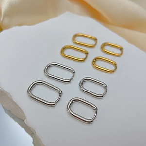 Minimalist oval stainless steel hoop earrings in gold and silver set on silk fabric