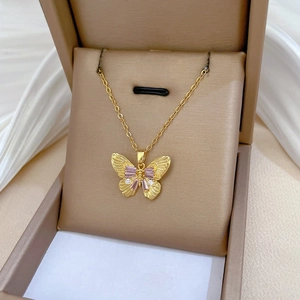 Detailed view of a gold titanium butterfly pendant with pink crystals on white fabric