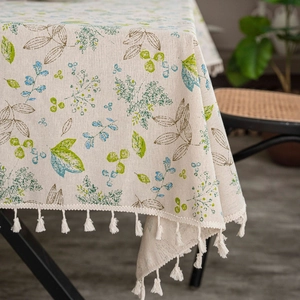 Detail of beige linen tablecloth with green leaf patterns and white fringe edges
