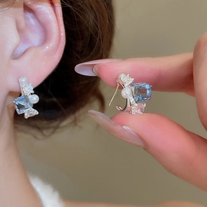 Close-up of bow earrings with blue crystal and white pearl on model's ear
